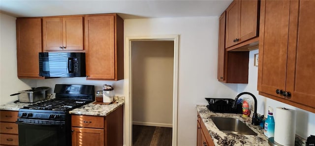 kitchen with light stone counters, sink, dark wood-type flooring, and black appliances