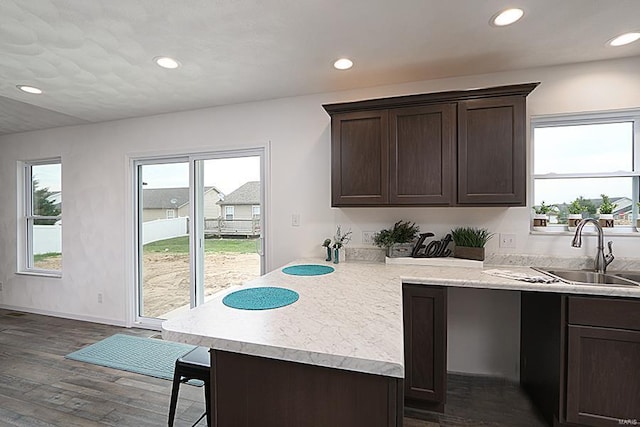 kitchen with sink, dark brown cabinets, dark hardwood / wood-style floors, and kitchen peninsula