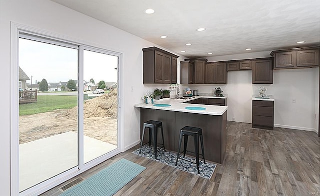 kitchen featuring sink, a kitchen bar, dark wood-type flooring, kitchen peninsula, and dark brown cabinets