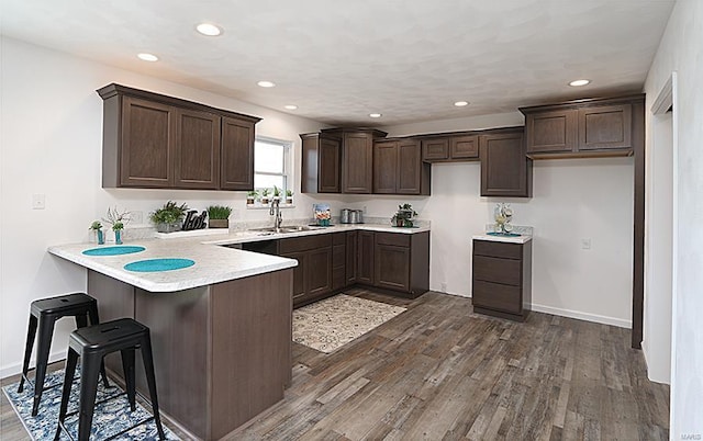 kitchen featuring a breakfast bar, dark hardwood / wood-style floors, sink, dark brown cabinetry, and kitchen peninsula