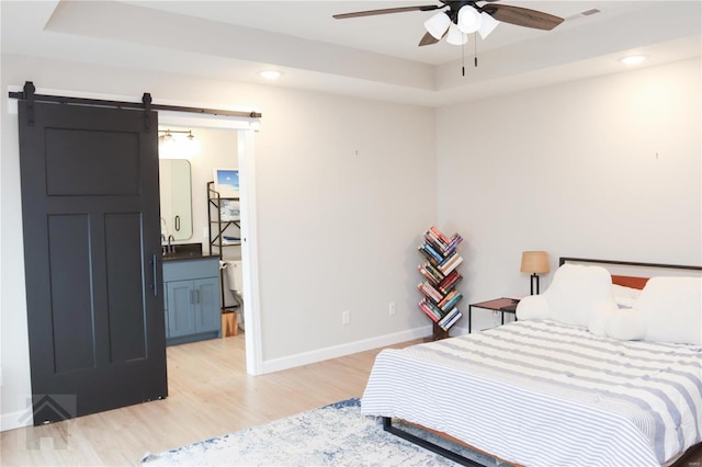 bedroom with light wood-style floors, a barn door, baseboards, and a raised ceiling