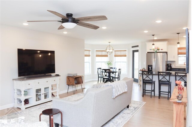 living area featuring baseboards, light wood finished floors, ceiling fan with notable chandelier, and recessed lighting