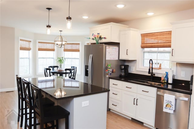 kitchen with a notable chandelier, stainless steel appliances, a sink, a kitchen breakfast bar, and white cabinets