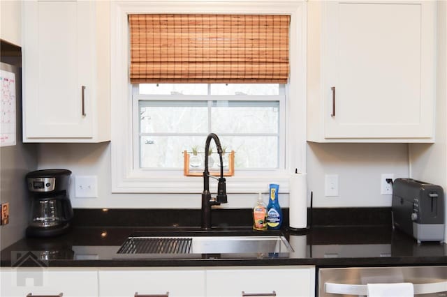 kitchen with dark countertops, white cabinetry, and a sink