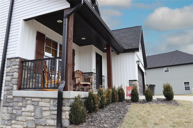 view of side of home with covered porch, stone siding, and roof with shingles