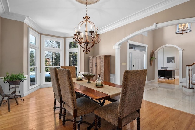 dining area with ornate columns, ornamental molding, an inviting chandelier, and light hardwood / wood-style flooring