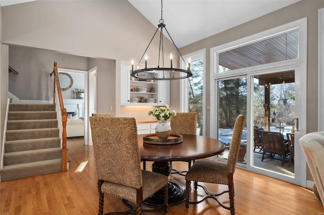 dining area with high vaulted ceiling, an inviting chandelier, and light hardwood / wood-style flooring