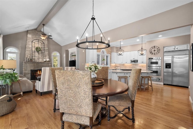 dining room with a stone fireplace, high vaulted ceiling, light hardwood / wood-style flooring, ceiling fan, and beam ceiling