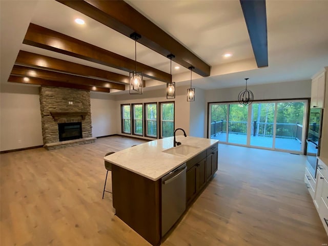 kitchen featuring white cabinetry, a center island with sink, sink, stainless steel dishwasher, and pendant lighting