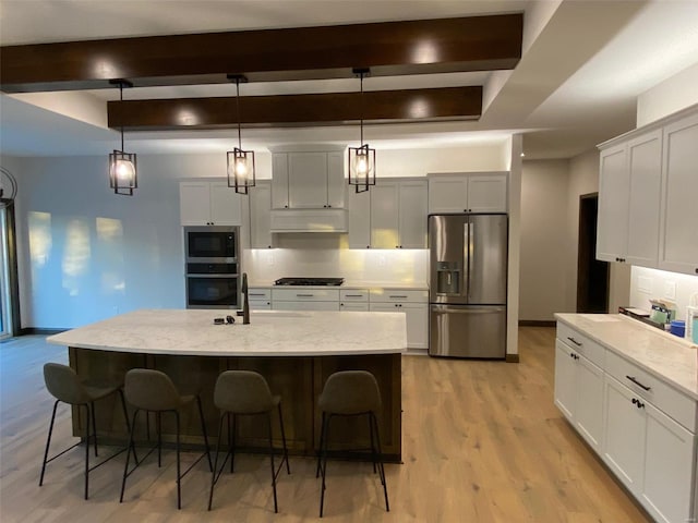 kitchen with a center island with sink, hanging light fixtures, a kitchen bar, and stainless steel appliances