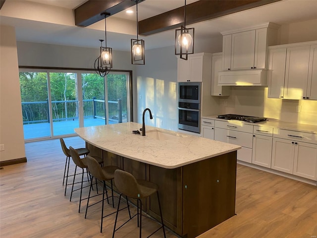 kitchen with appliances with stainless steel finishes, hanging light fixtures, an island with sink, white cabinets, and sink