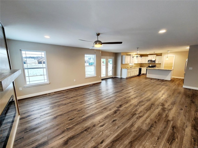 unfurnished living room with ceiling fan, a wealth of natural light, and dark hardwood / wood-style flooring