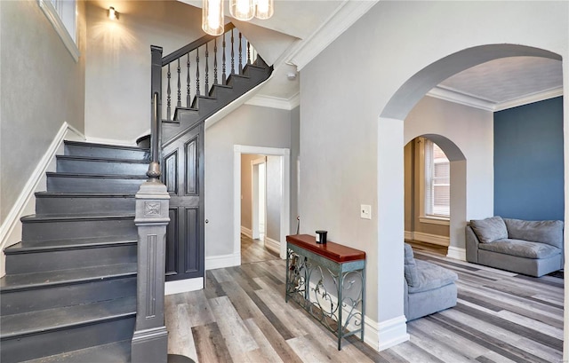 stairway featuring a towering ceiling, wood-type flooring, and ornamental molding