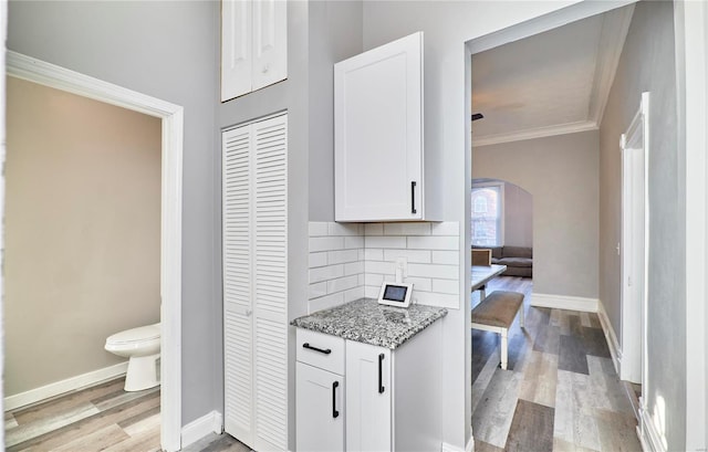 kitchen featuring light hardwood / wood-style flooring, white cabinetry, ornamental molding, light stone countertops, and decorative backsplash