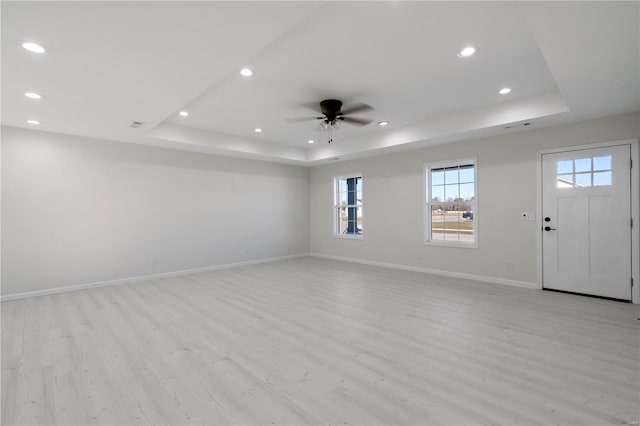 unfurnished room with ceiling fan, a tray ceiling, and light hardwood / wood-style floors