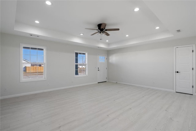 empty room with ceiling fan, a tray ceiling, and light wood-type flooring