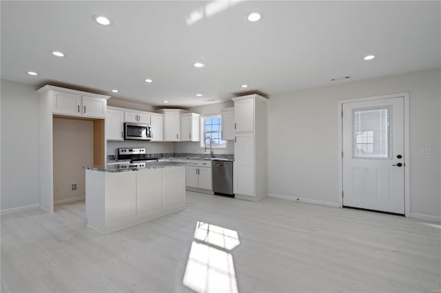 kitchen with sink, white cabinetry, dark stone countertops, stainless steel appliances, and a center island