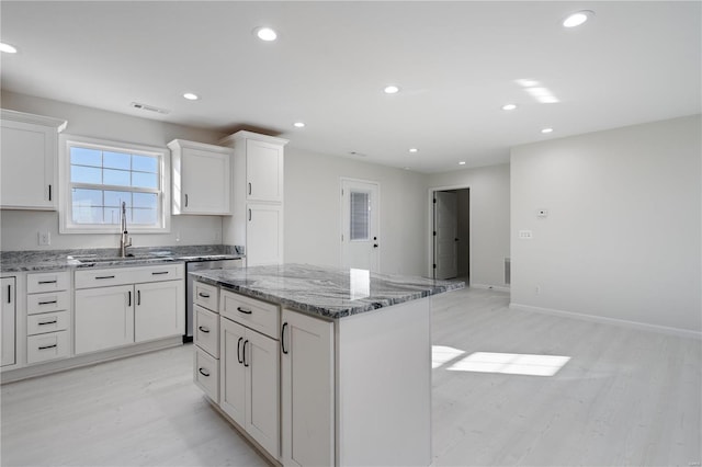 kitchen with sink, light stone counters, light hardwood / wood-style floors, white cabinets, and a kitchen island