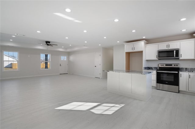 kitchen featuring white cabinetry, a center island, appliances with stainless steel finishes, ceiling fan, and light stone countertops