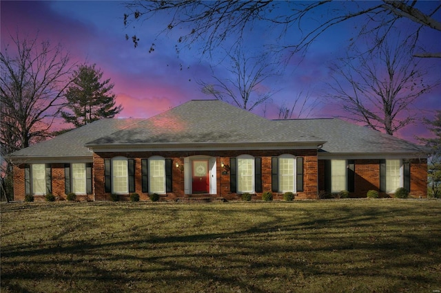 view of front of home featuring roof with shingles, a lawn, and brick siding