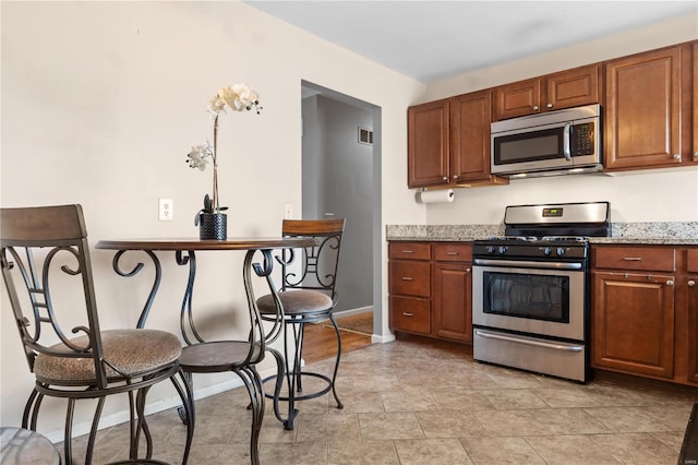 kitchen with appliances with stainless steel finishes, brown cabinetry, baseboards, and light stone countertops