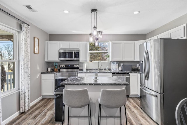 kitchen featuring appliances with stainless steel finishes, hanging light fixtures, a center island, white cabinets, and a kitchen bar