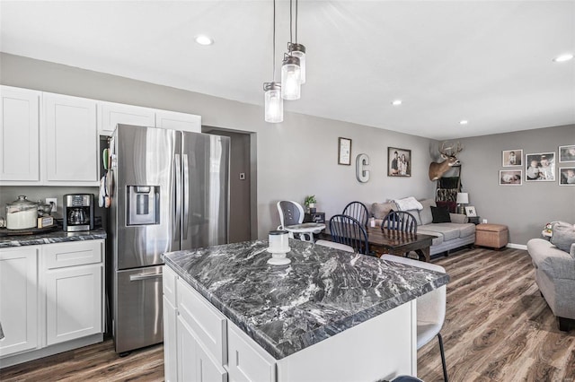 kitchen with a kitchen island, decorative light fixtures, white cabinetry, stainless steel fridge, and dark stone counters