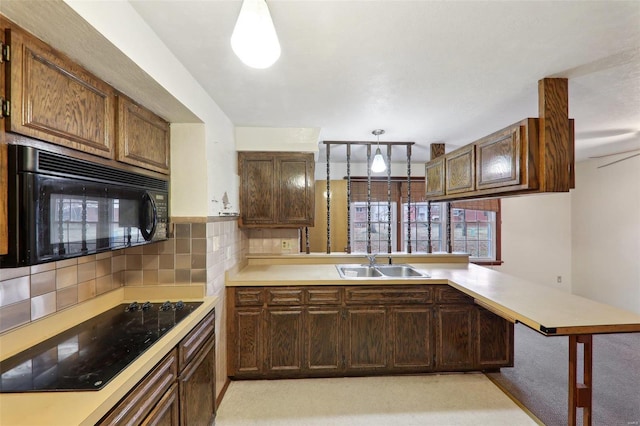 kitchen featuring kitchen peninsula, decorative light fixtures, sink, a kitchen breakfast bar, and black appliances