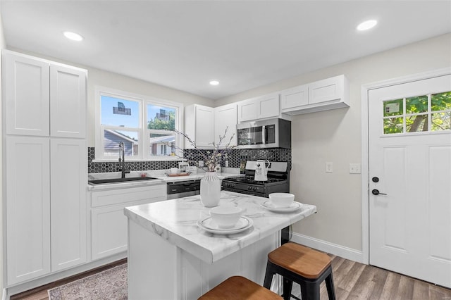 kitchen with white cabinetry, stainless steel appliances, a kitchen bar, and sink