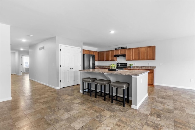 kitchen with range with electric cooktop, stainless steel fridge, a breakfast bar area, and a center island with sink