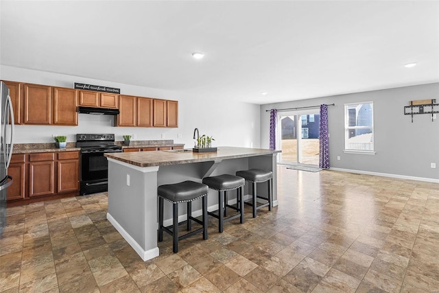 kitchen featuring black electric range oven, a breakfast bar area, stainless steel refrigerator, and a center island with sink