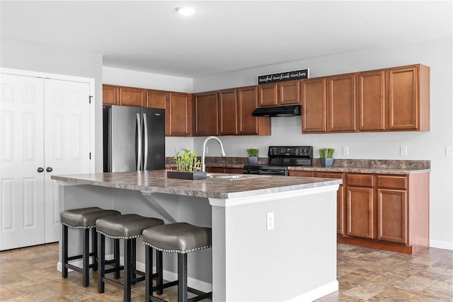 kitchen featuring a kitchen bar, sink, stainless steel refrigerator, black range with electric stovetop, and a kitchen island with sink