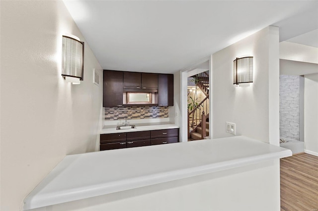 kitchen featuring dark brown cabinets, sink, backsplash, and light hardwood / wood-style flooring