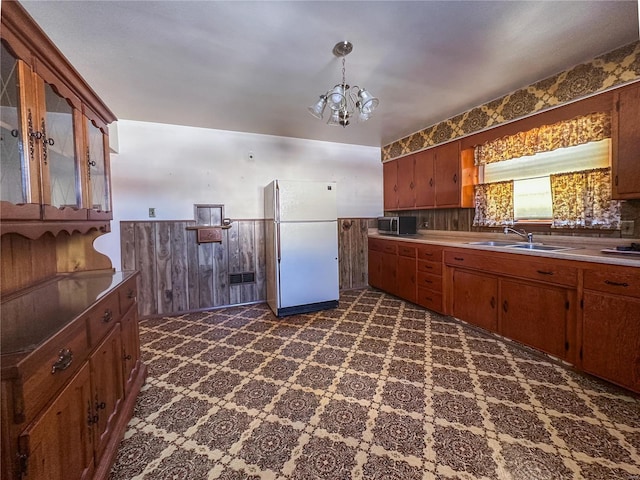 kitchen with white fridge, sink, a notable chandelier, and wood walls