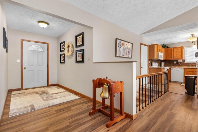 foyer with sink, vaulted ceiling, light hardwood / wood-style floors, and a textured ceiling