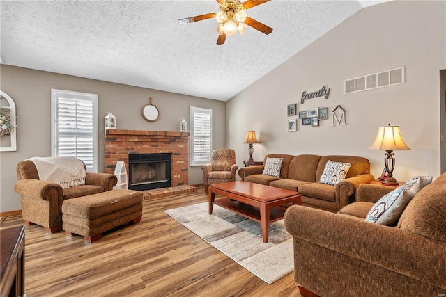 living room featuring a fireplace, vaulted ceiling, a textured ceiling, and light hardwood / wood-style flooring