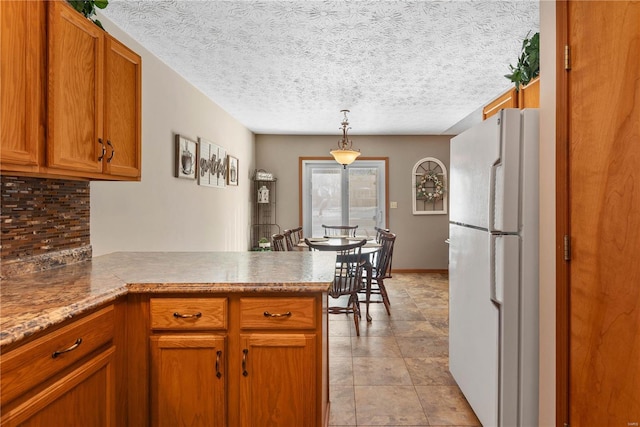 kitchen with hanging light fixtures, white fridge, a textured ceiling, and kitchen peninsula