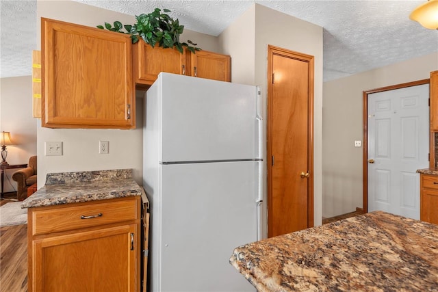 kitchen featuring white refrigerator, a textured ceiling, and dark stone counters