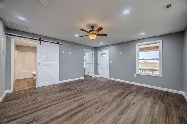 spare room featuring dark wood-type flooring, ceiling fan, and a barn door