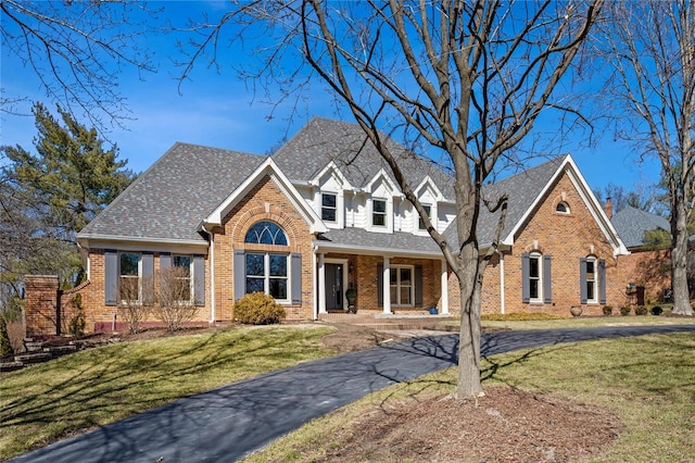 view of front facade with brick siding, driveway, a front lawn, and roof with shingles