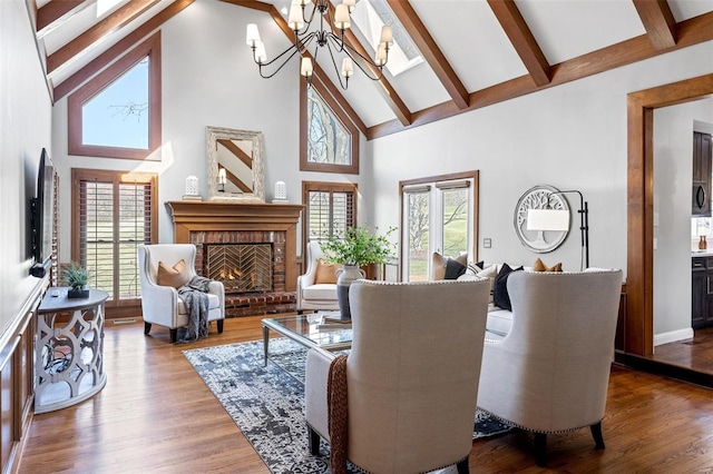 living room with wood finished floors, beamed ceiling, a fireplace, high vaulted ceiling, and a notable chandelier