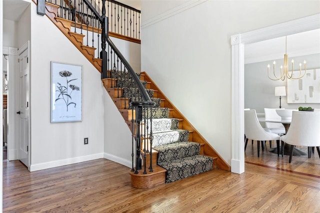 staircase featuring baseboards, crown molding, wood finished floors, and an inviting chandelier