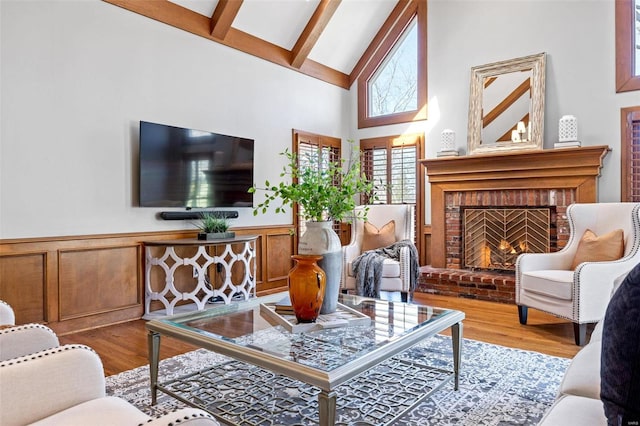 living area featuring a wainscoted wall, beamed ceiling, wood finished floors, a fireplace, and high vaulted ceiling