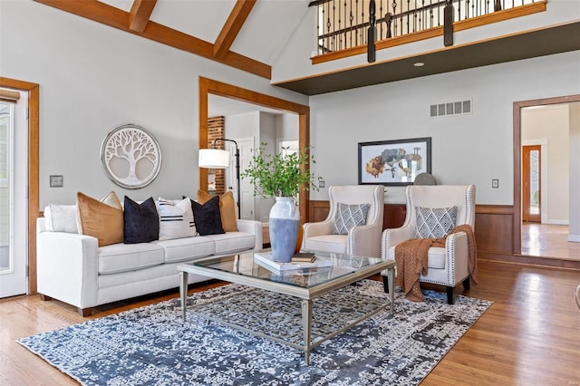 living room with beam ceiling, visible vents, wainscoting, wood finished floors, and high vaulted ceiling