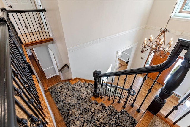 stairway with a high ceiling, wood finished floors, and a notable chandelier