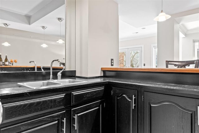 kitchen with dark countertops, ornamental molding, dark cabinets, pendant lighting, and a sink