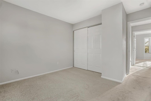 unfurnished bedroom featuring a closet, light colored carpet, and baseboards