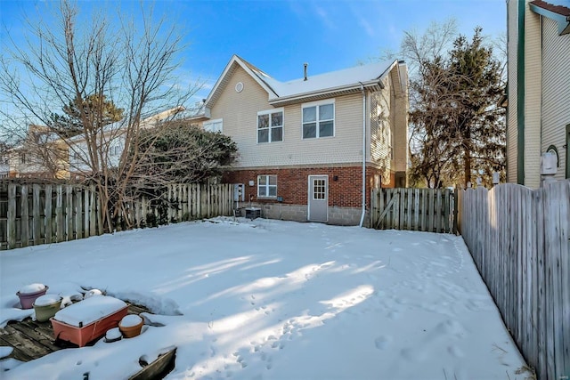 snow covered house with brick siding, a chimney, and a fenced backyard