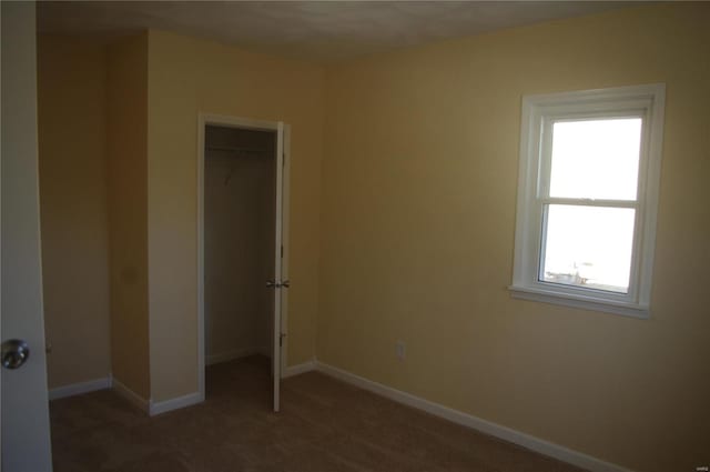 unfurnished bedroom featuring multiple windows, dark carpet, and a closet