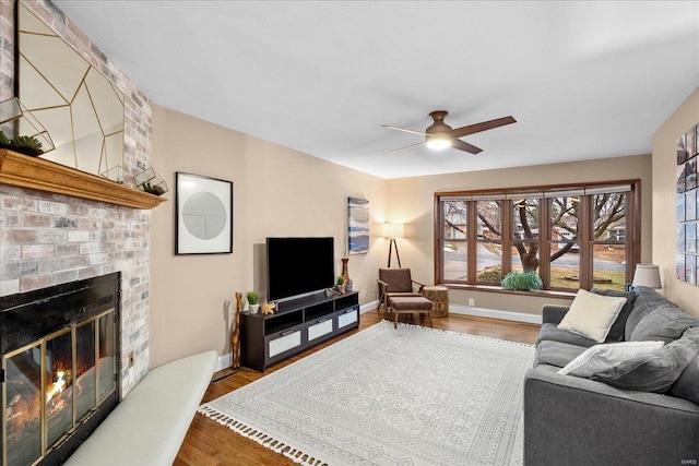 living room featuring a brick fireplace, wood-type flooring, and ceiling fan